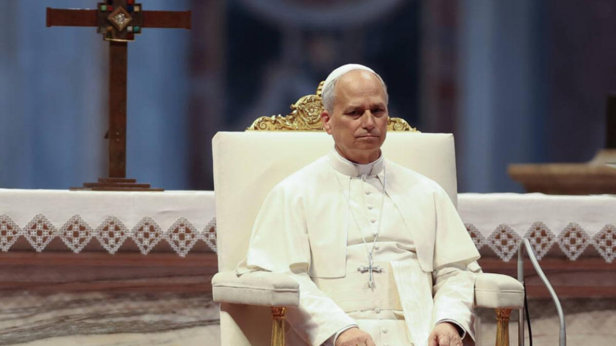 Pope in white robes sitting on an ornate chair in a church setting with an altar behind him