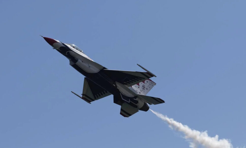 Fighter jet performing an airshow maneuver, blue sky with a white smoke trail behind it