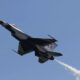 Fighter jet performing an airshow maneuver, blue sky with a white smoke trail behind it