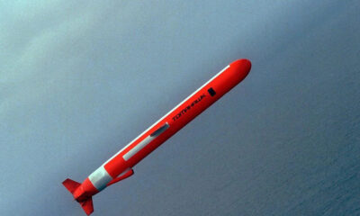 Red rocket streaking upward diagonally over a blue sea horizon.