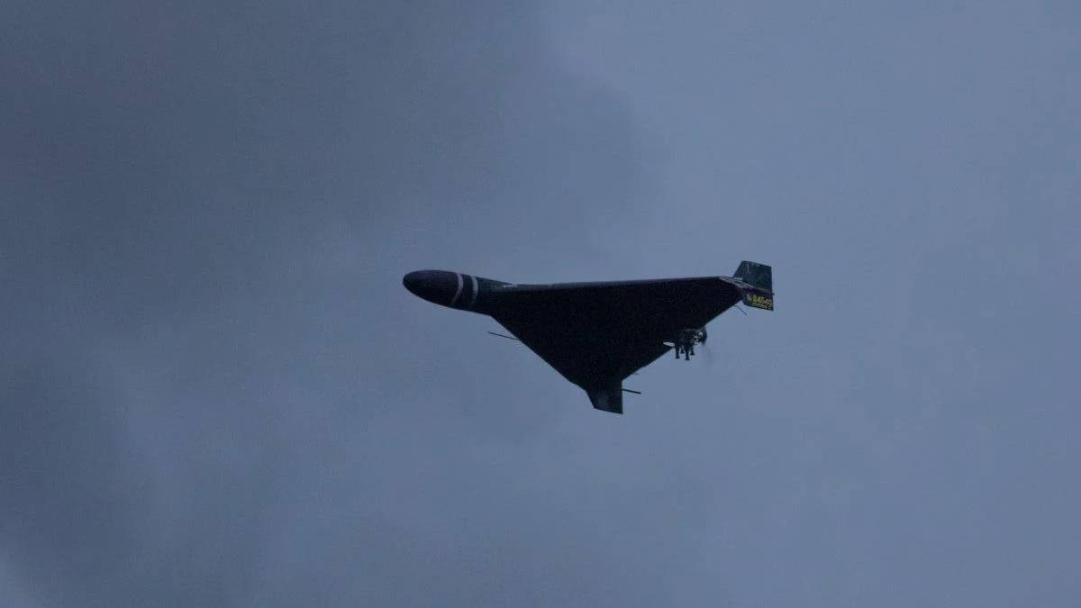 Dark triangular stealth bomber flying wing silhouette against a cloudy blue sky, with landing gear extended cradled beneath.