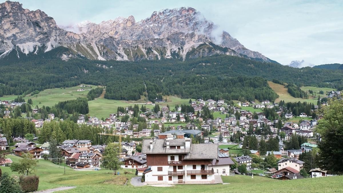 Alpine village with chalet-style houses in a green valley and rocky mountains in the background.