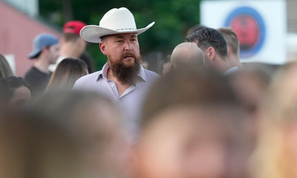 Bearded man in a white cowboy hat among a crowd at an outdoor event.