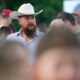 Bearded man in a white cowboy hat among a crowd at an outdoor event.