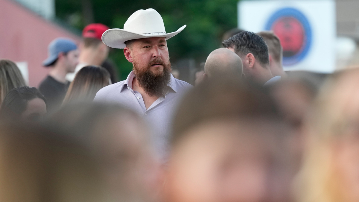 Bearded man in a white cowboy hat among a crowd at an outdoor event.