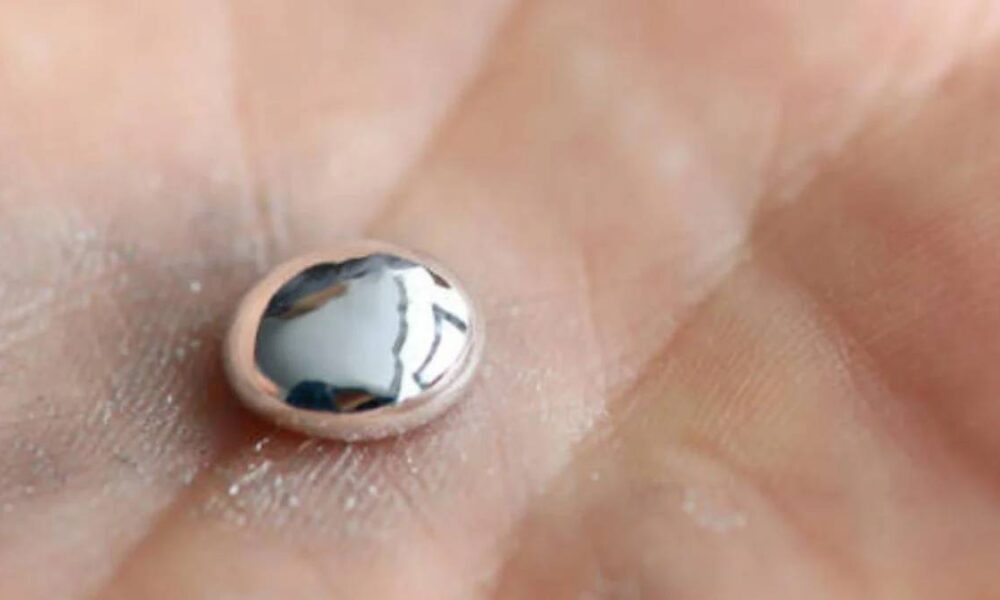Tiny dome-shaped, pearl-like bead resting on the palm of a hand, reflecting light.
