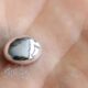 Tiny dome-shaped, pearl-like bead resting on the palm of a hand, reflecting light.