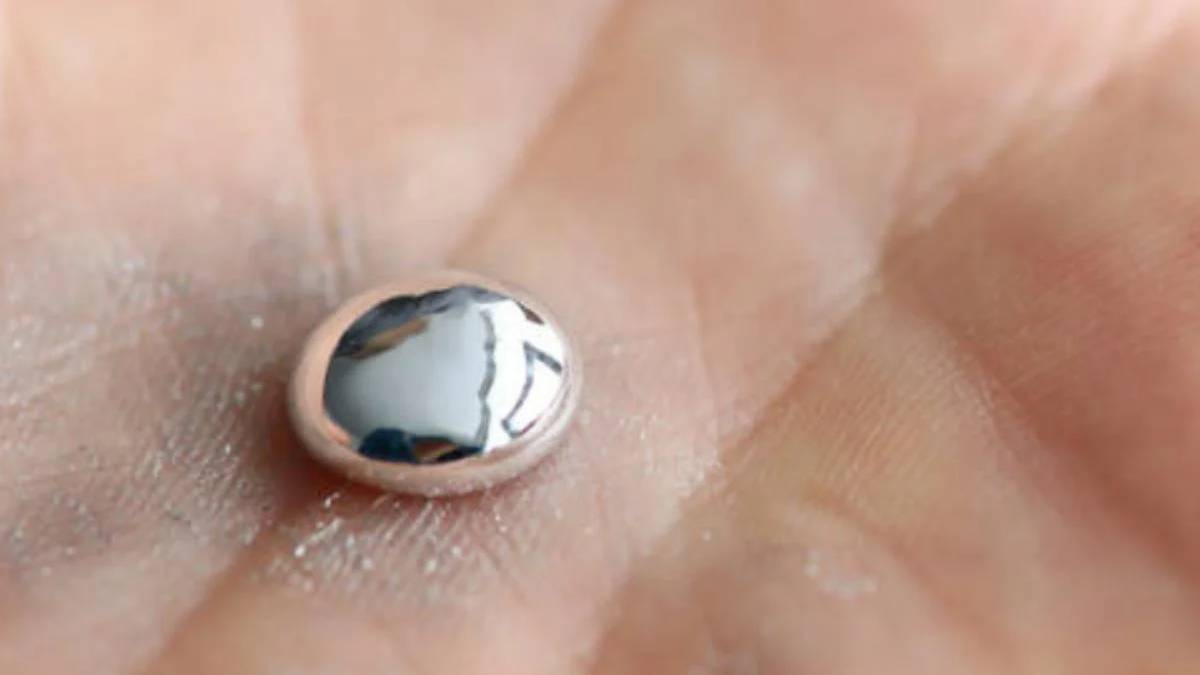 Tiny dome-shaped, pearl-like bead resting on the palm of a hand, reflecting light.