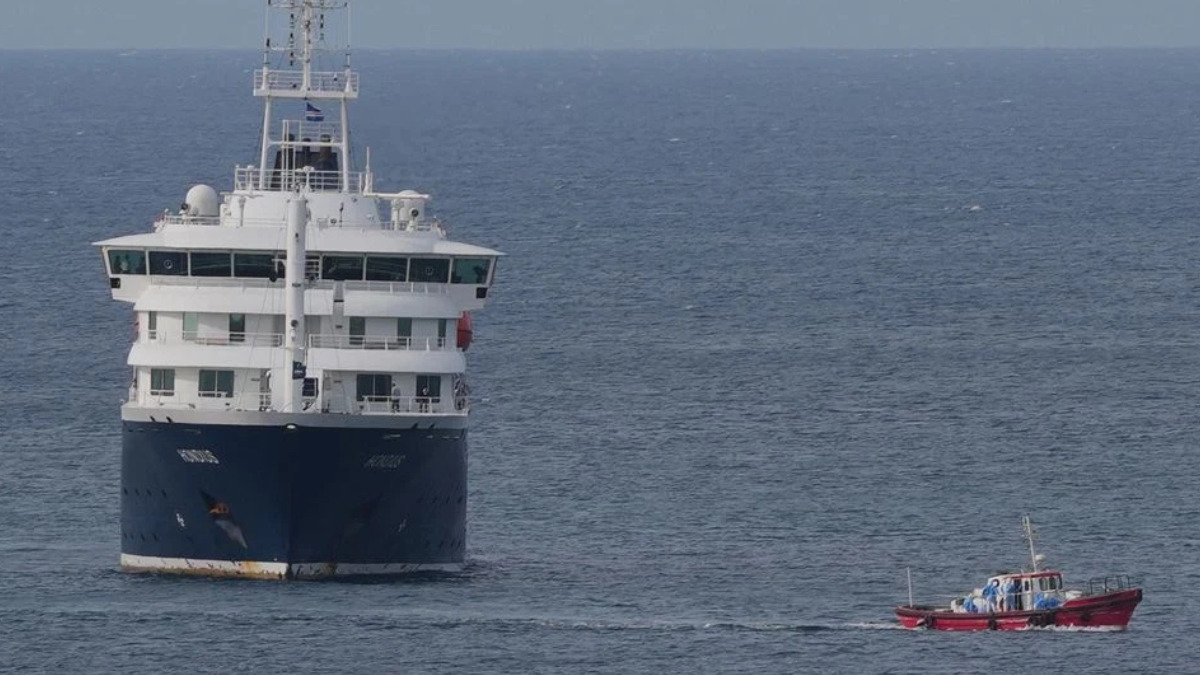 Large white and blue passenger ferry on calm open water, with a small red boat nearby for scale and support.