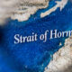Close-up of a map highlighting the Strait of Hormuz, with blue ocean and surrounding beige land.