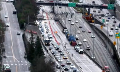 Overhead view of a busy multi-lane freeway with a construction zone in the middle, orange cones, and line of vehicles behind them.