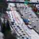 Overhead view of a busy multi-lane freeway with a construction zone in the middle, orange cones, and line of vehicles behind them.