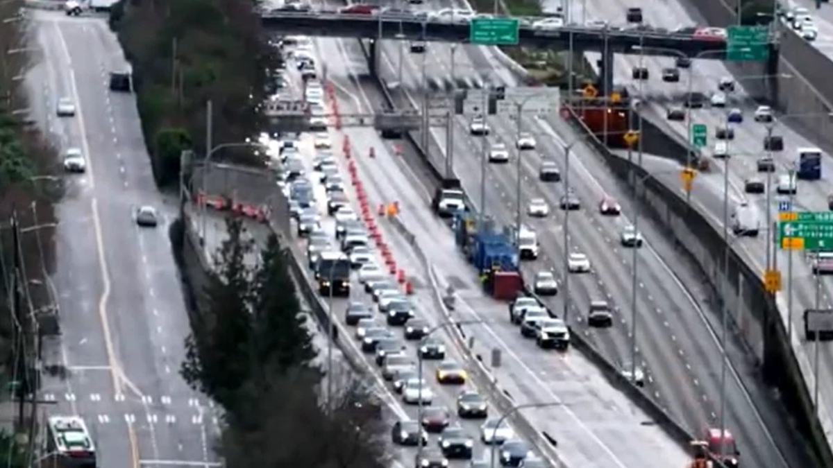 Overhead view of a busy multi-lane freeway with a construction zone in the middle, orange cones, and line of vehicles behind them.