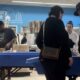 Shoppers gather around a blue display table in a home improvement store, inspecting items as a staff member assists nearby.