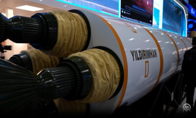 Large rocket engine on display with white fuselage and orange stripes labeled YILDIRIMHAN; visitors and screens in the background.