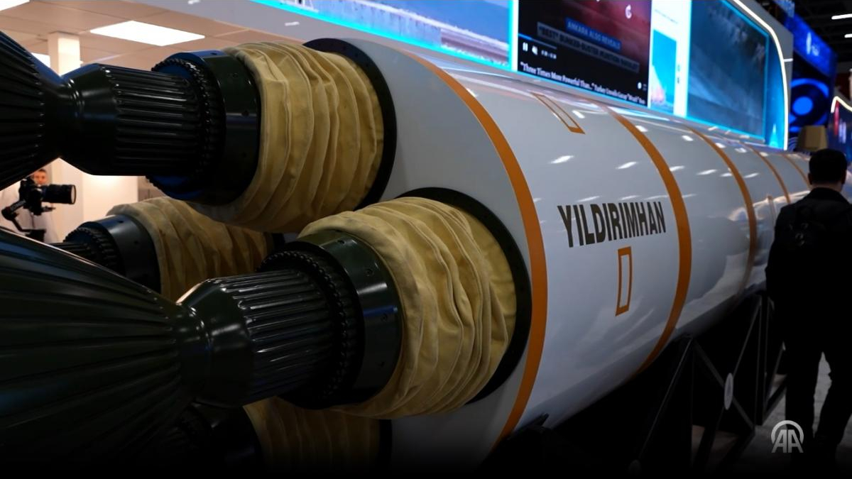 Large rocket engine on display with white fuselage and orange stripes labeled YILDIRIMHAN; visitors and screens in the background.