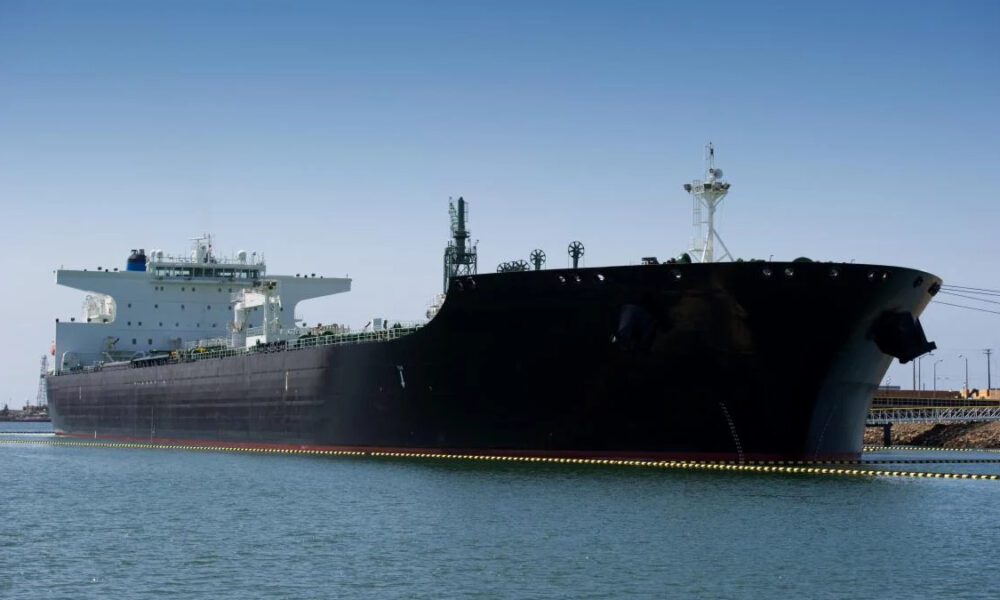 Large black oil tanker moored in a calm harbor under a clear blue sky.