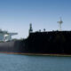 Large black oil tanker moored in a calm harbor under a clear blue sky.