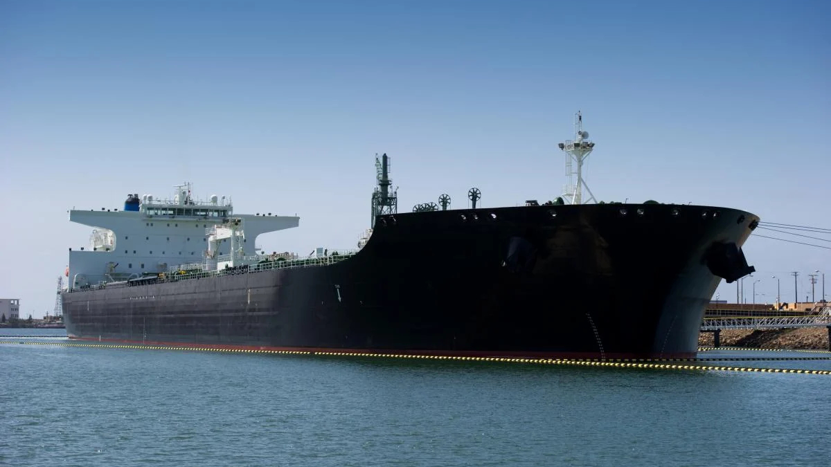 Large black oil tanker moored in a calm harbor under a clear blue sky.