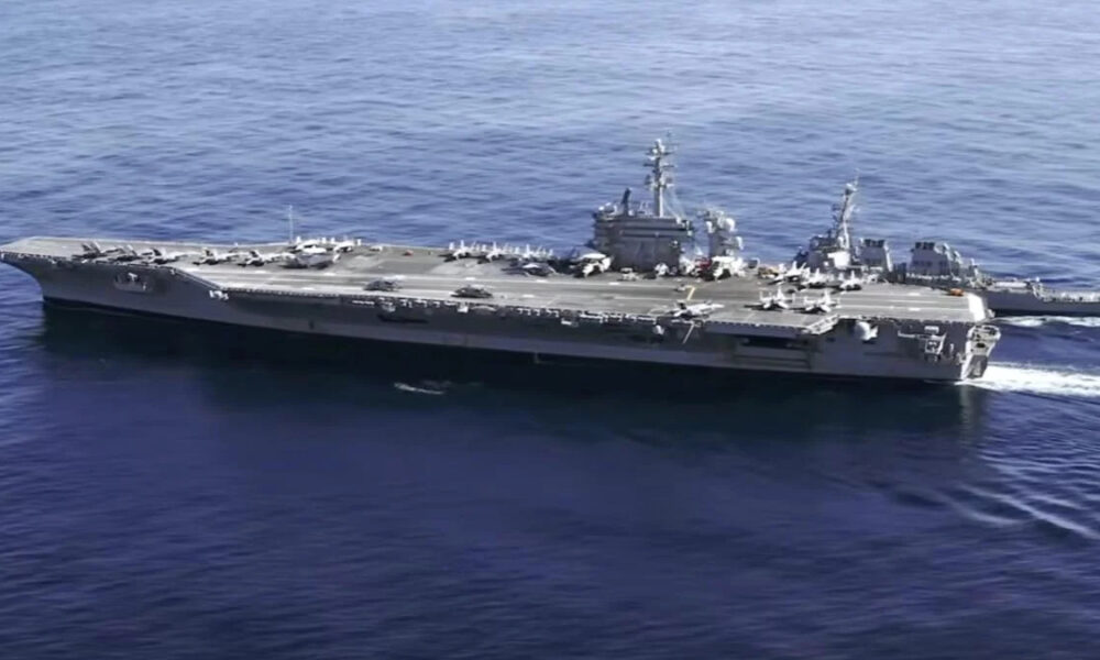 Aircraft carrier at sea with aircraft on its deck and a support vessel nearby.