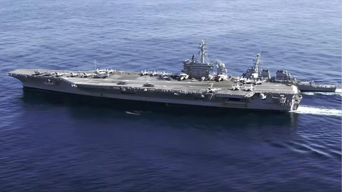 Aircraft carrier at sea with aircraft on its deck and a support vessel nearby.