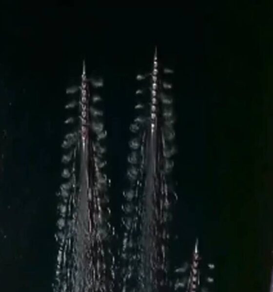 Aerial view of a rowing race on a dark river with multiple long boats and crowded shores on both sides.