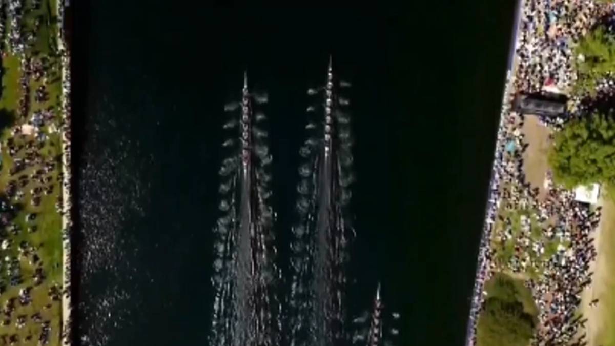Aerial view of a rowing race on a dark river with multiple long boats and crowded shores on both sides.