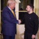 Two men shake hands in an opulent, gold-trimmed room with cream furniture and tall gold curtains in the background.