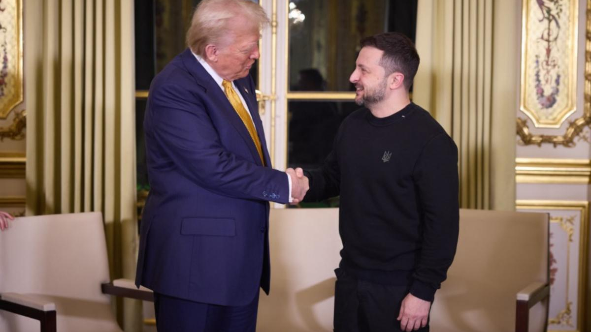 Two men shake hands in an opulent, gold-trimmed room with cream furniture and tall gold curtains in the background.