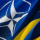 Flags of NATO and Ukraine waving together: blue flag with white NATO emblem beside a blue-and-yellow Ukrainian flag, symbolizing alliance and support.