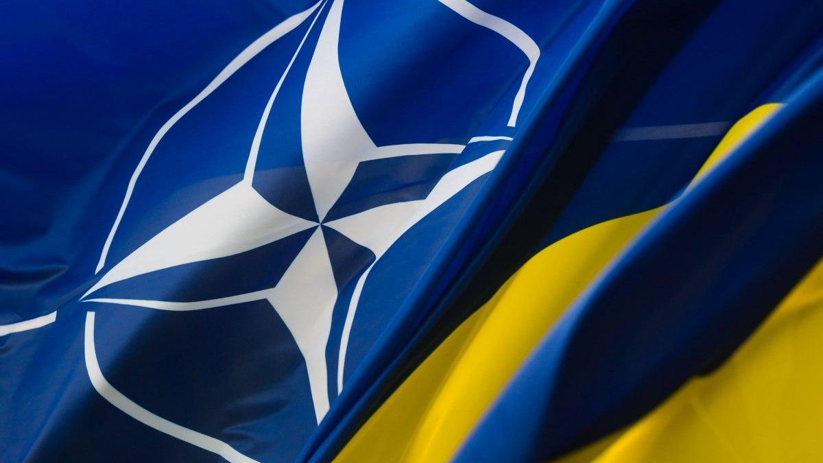 Flags of NATO and Ukraine waving together: blue flag with white NATO emblem beside a blue-and-yellow Ukrainian flag, symbolizing alliance and support.