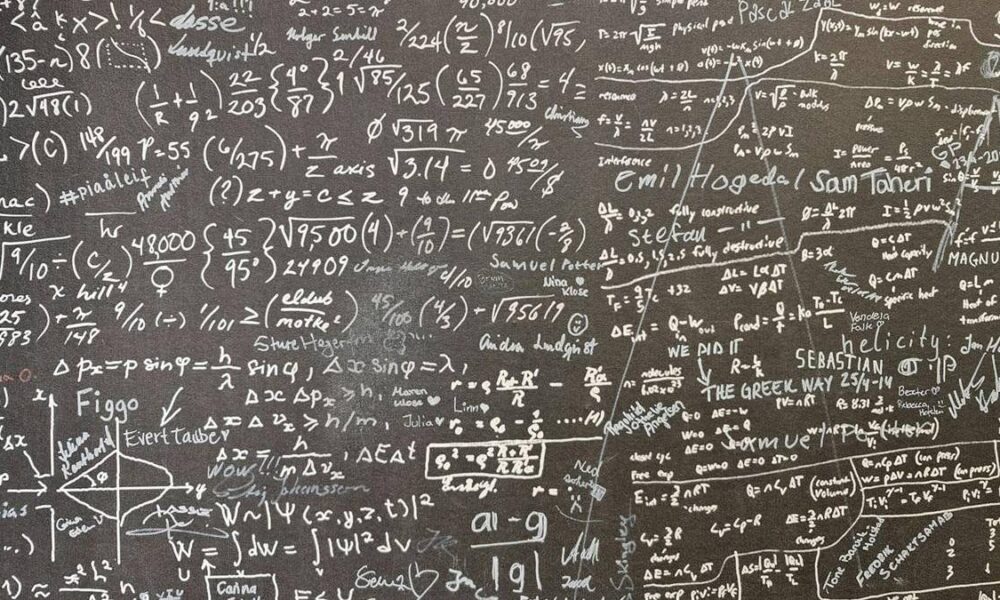 Chalkboard filled with complex mathematical equations, formulas, and diagrams written in white chalk on a dark surface.