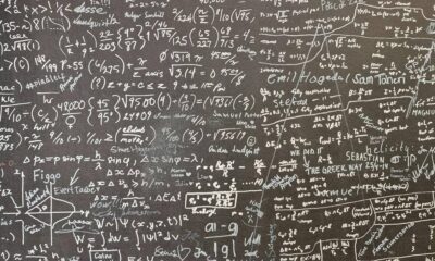 Chalkboard filled with complex mathematical equations, formulas, and diagrams written in white chalk on a dark surface.
