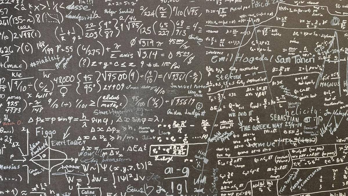 Chalkboard filled with complex mathematical equations, formulas, and diagrams written in white chalk on a dark surface.