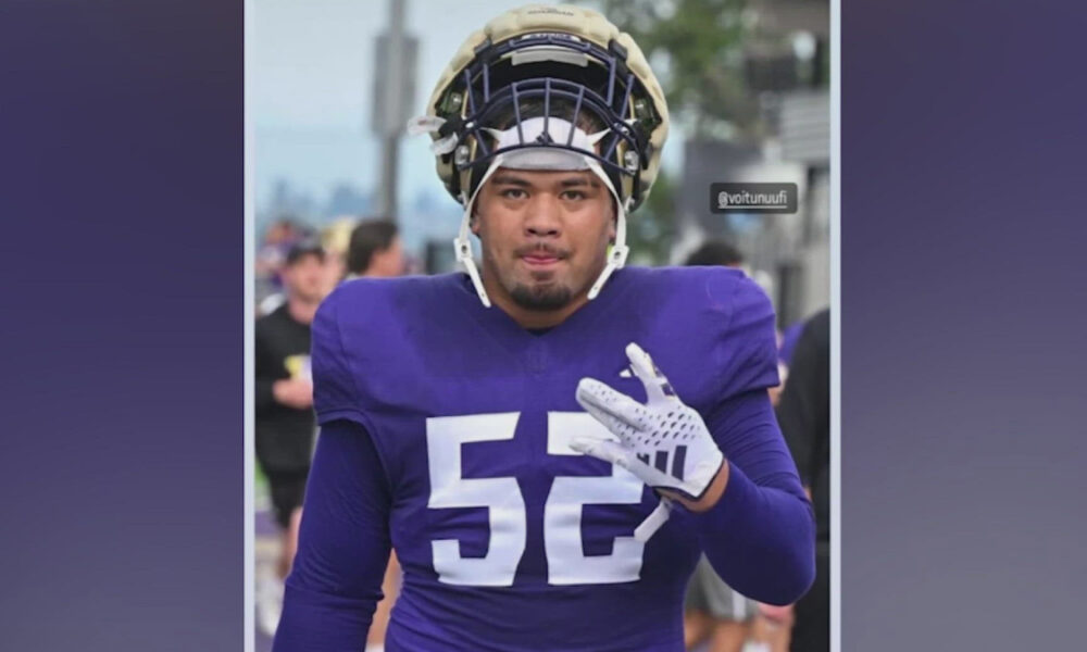 Football player wearing a purple jersey with number 52, helmet on, walking outdoors and gesturing with his right hand.