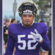 Football player wearing a purple jersey with number 52, helmet on, walking outdoors and gesturing with his right hand.
