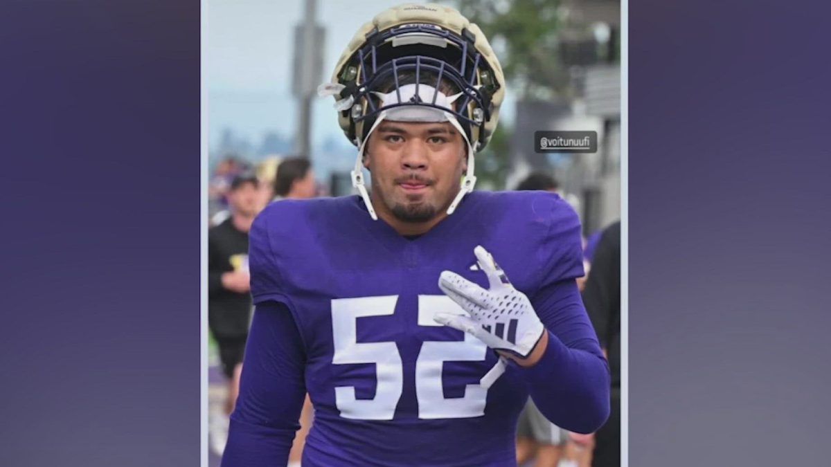 Football player wearing a purple jersey with number 52, helmet on, walking outdoors and gesturing with his right hand.