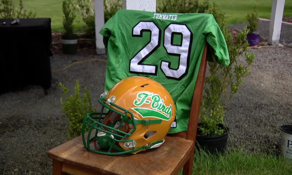 Green football jersey with the number 29 draped over a chair, beside an orange and green T-Birds helmet outdoors.
