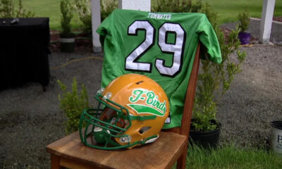 Green football jersey with the number 29 draped over a chair, beside an orange and green T-Birds helmet outdoors.