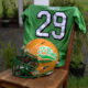 Green football jersey with the number 29 draped over a chair, beside an orange and green T-Birds helmet outdoors.