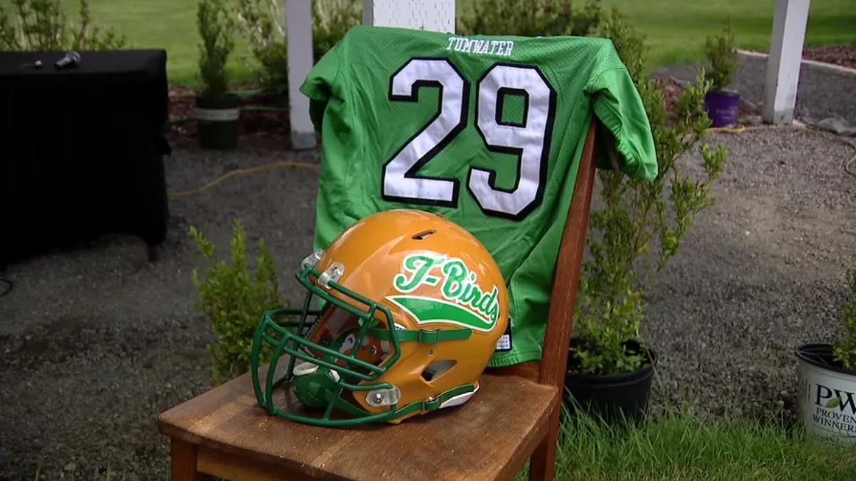 Green football jersey with the number 29 draped over a chair, beside an orange and green T-Birds helmet outdoors.