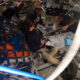 Astronauts seated and working around a central console in a cramped spacecraft cabin, with tablets and equipment visible and a NASA label in the corner.
