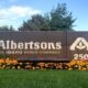 Albertsons sign at entrance with flower bed, Idaho-based company and 250th anniversary logo visible
