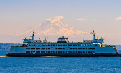 Large white passenger ferry sailing on calm blue water with a snow‑capped mountain in the background.
