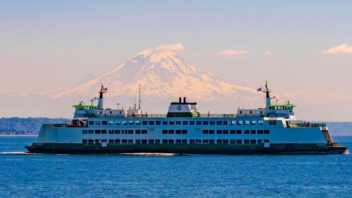 Large white passenger ferry sailing on calm blue water with a snow‑capped mountain in the background.