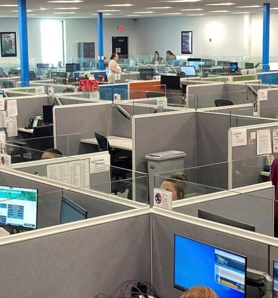 Open-plan call center with gray cubicles, blue support columns, and staff working at computer desks.