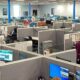 Open-plan call center with gray cubicles, blue support columns, and staff working at computer desks.