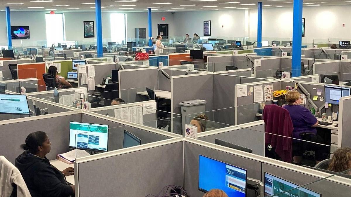Open-plan call center with gray cubicles, blue support columns, and staff working at computer desks.