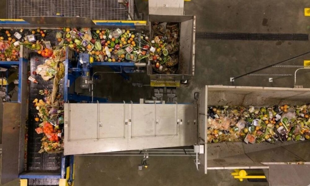 Top-down view of a waste-sorting facility with multiple conveyor belts and heaps of mixed recyclables and trash on a metal chute system.