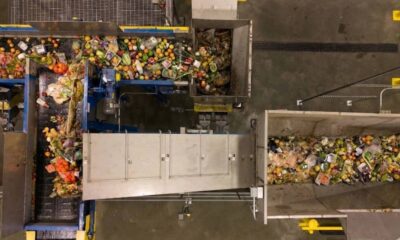 Top-down view of a waste-sorting facility with multiple conveyor belts and heaps of mixed recyclables and trash on a metal chute system.
